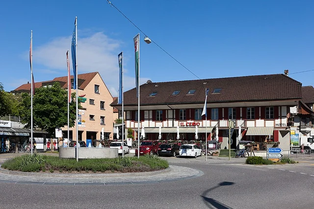Hirschenplatz con rotatoria e bandiere nel centro di Lyss – rappresentazione sfocata